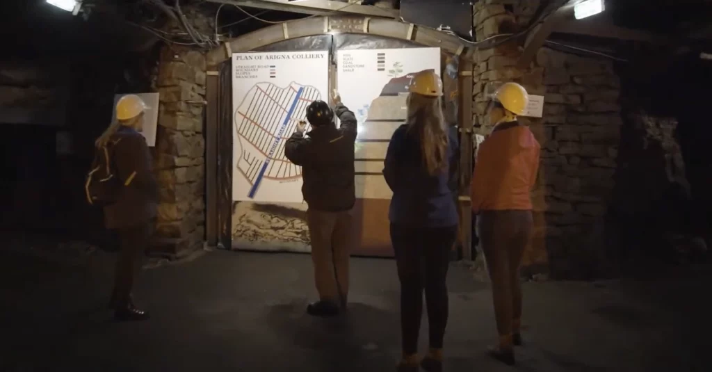 Visitors wearing helmets gather around a map of Arigna Colliery, learning about the mine layout during a guided tour.
