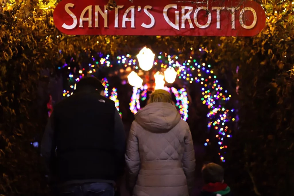 Family entering a brightly decorated pathway leading to Santa's Grotto, surrounded by colourful lights and greenery.