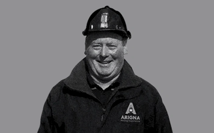 Smiling man wearing a helmet and jacket with the Arigna Mining Experience logo, promoting the mining heritage of Ireland.